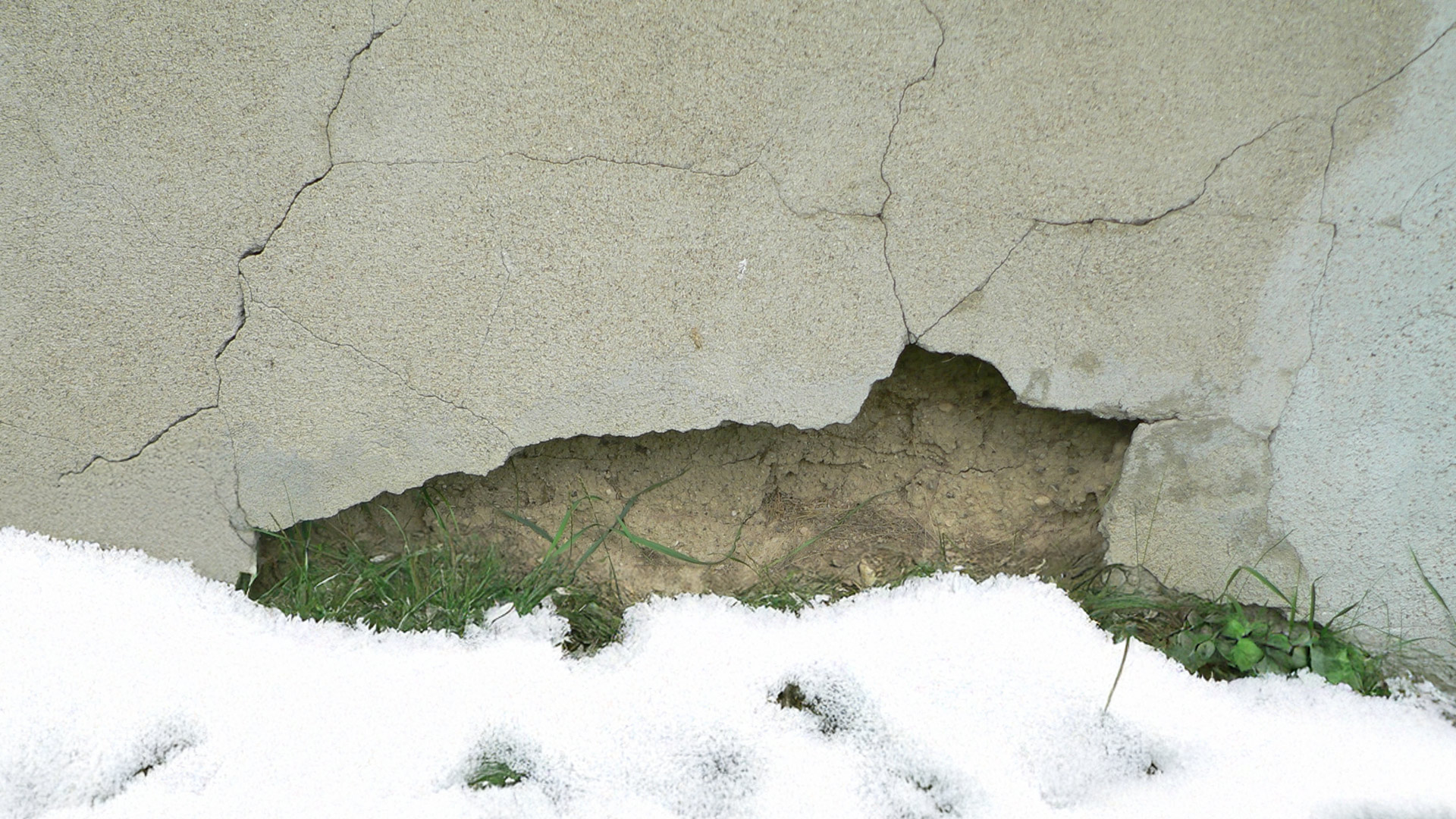 A damaged stucco wall with winter snow at the root of the problem.